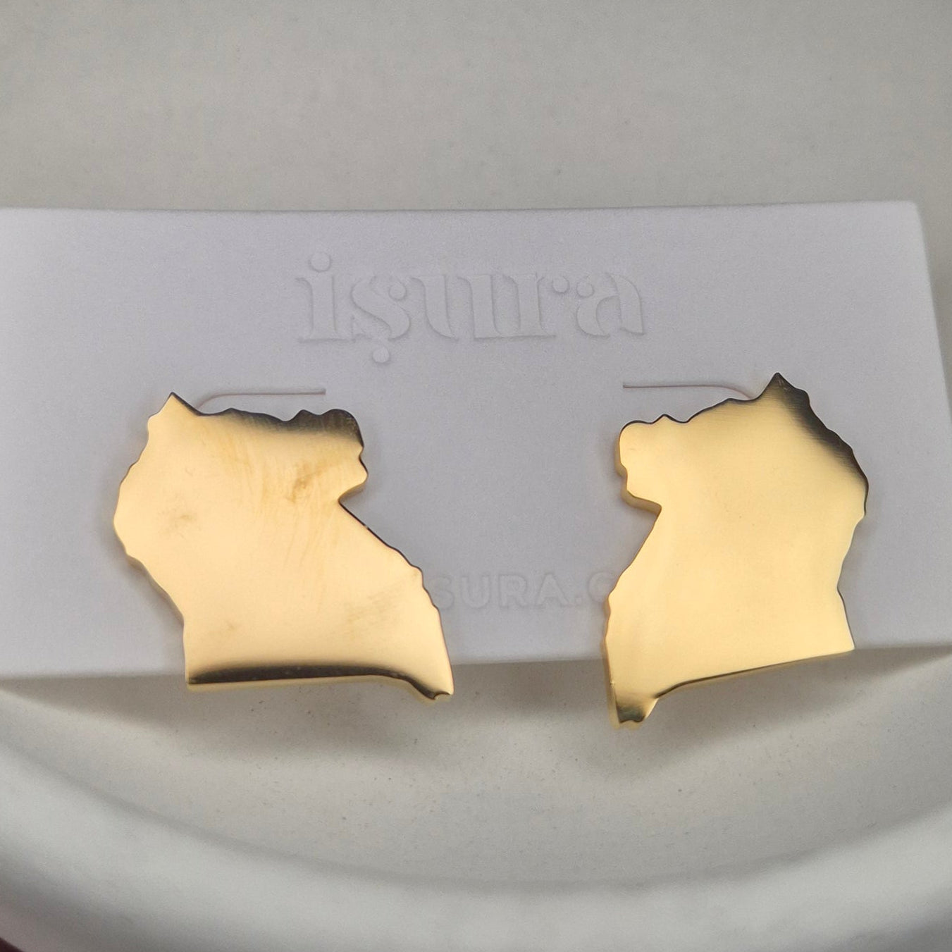 Gold earrings on a white card held in a hand with a blurred background
