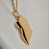 Gold necklace with a leaf-shaped pendant on a white surface