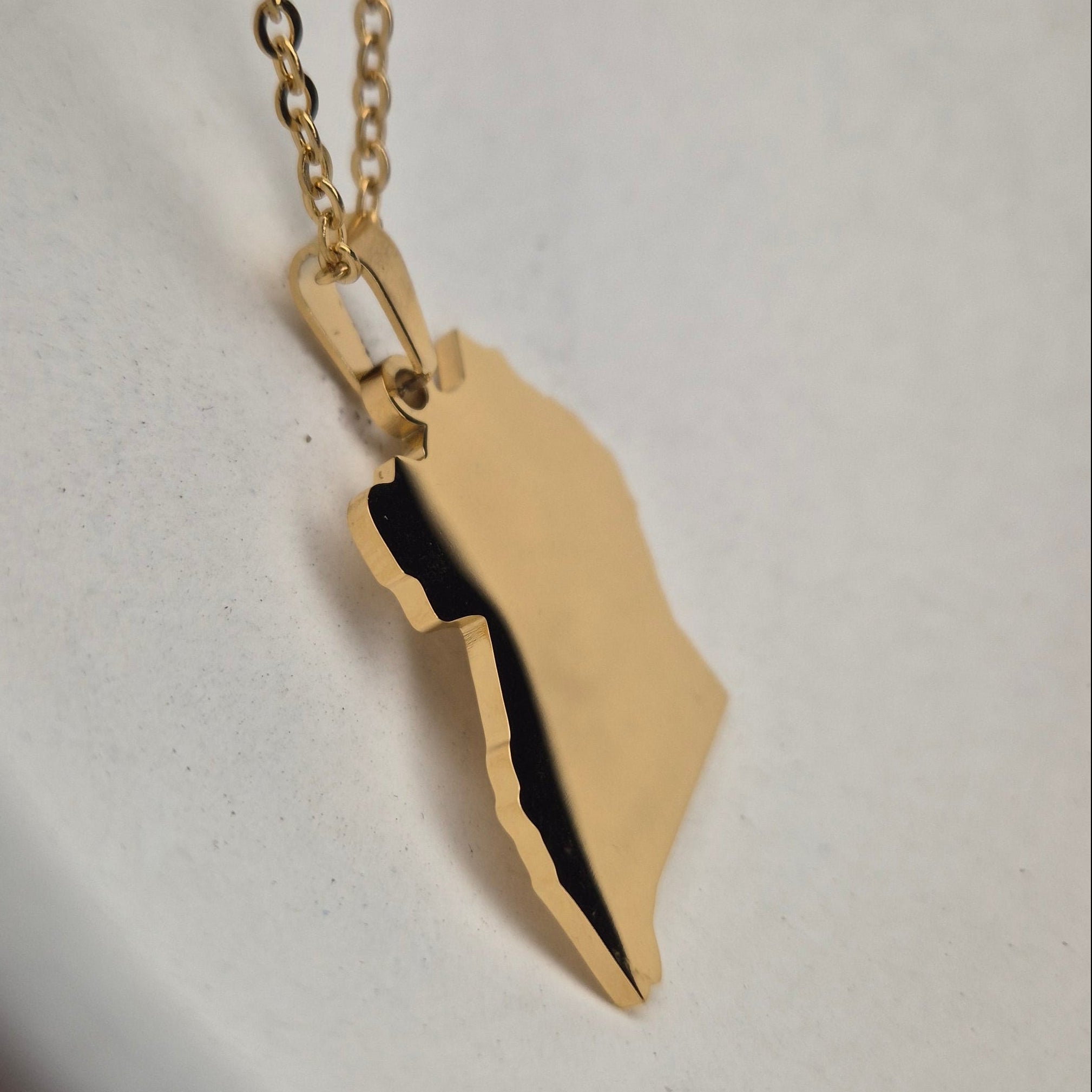 Gold necklace with a leaf-shaped pendant on a white surface