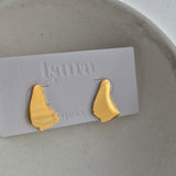 Gold Barbados map-shaped earrings on a white card with 'Isura' branding, placed on a textured surface.