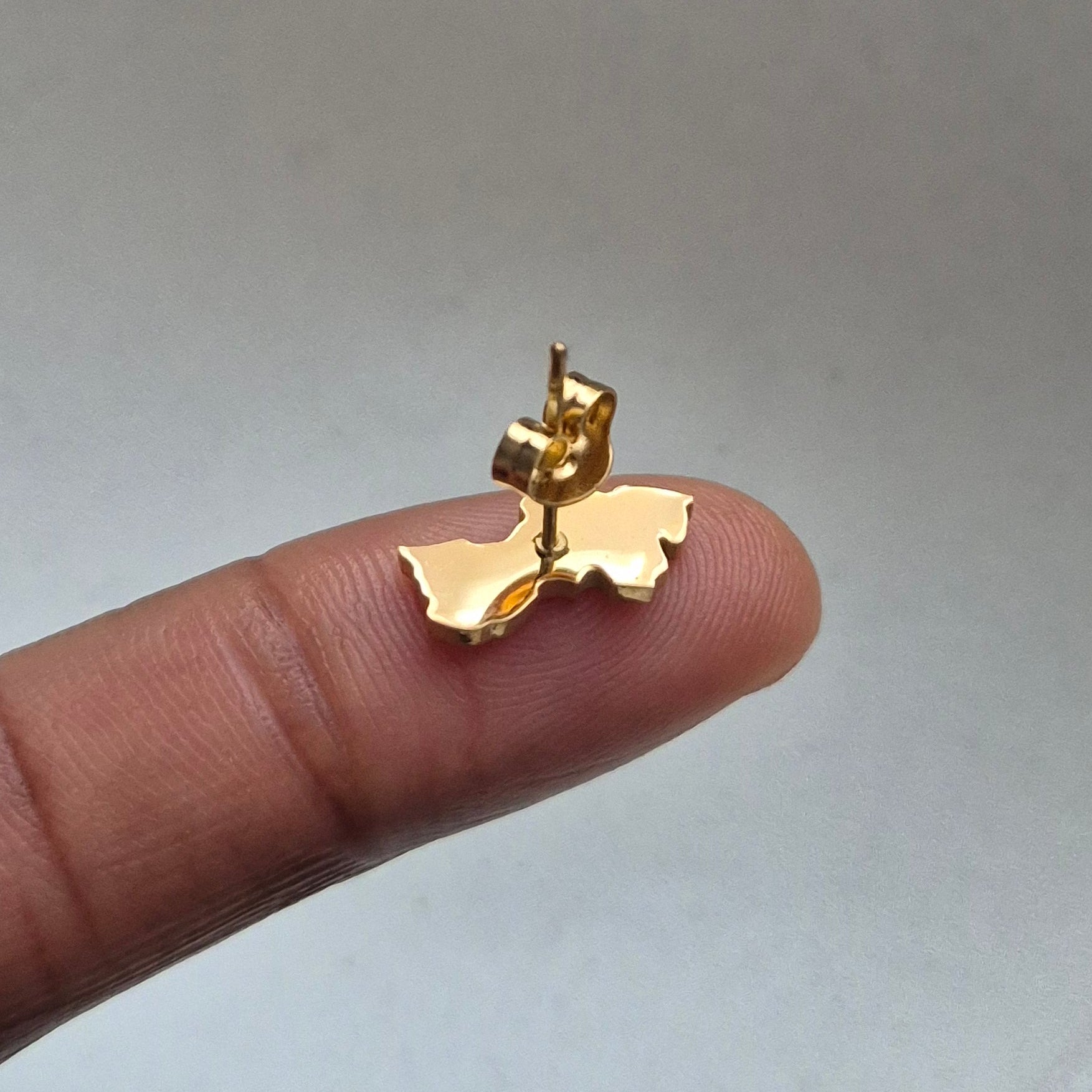 Gold Guyana map-shaped earring on a finger against a neutral background