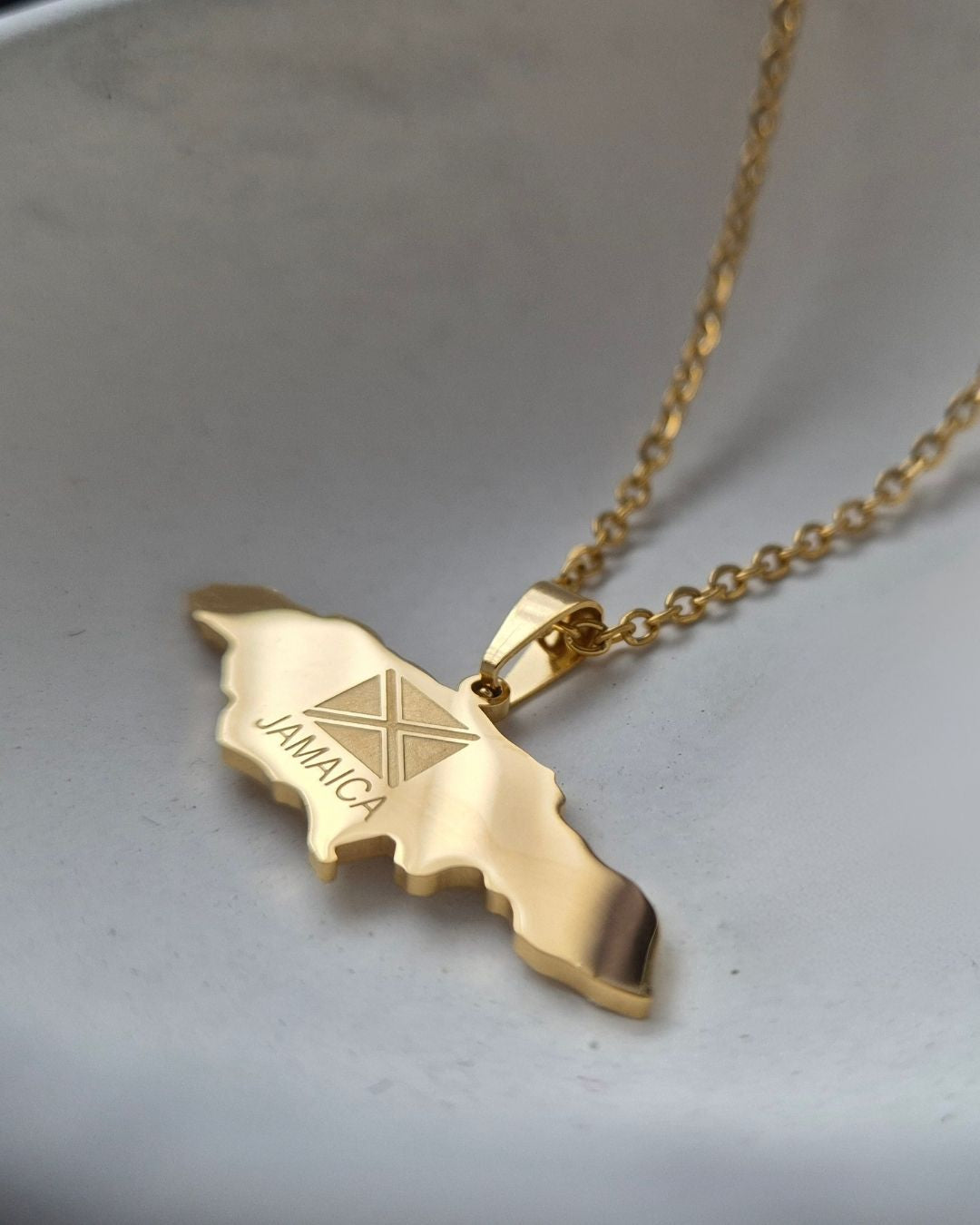Gold necklace with a map of Jamaica pendant on a light gray background