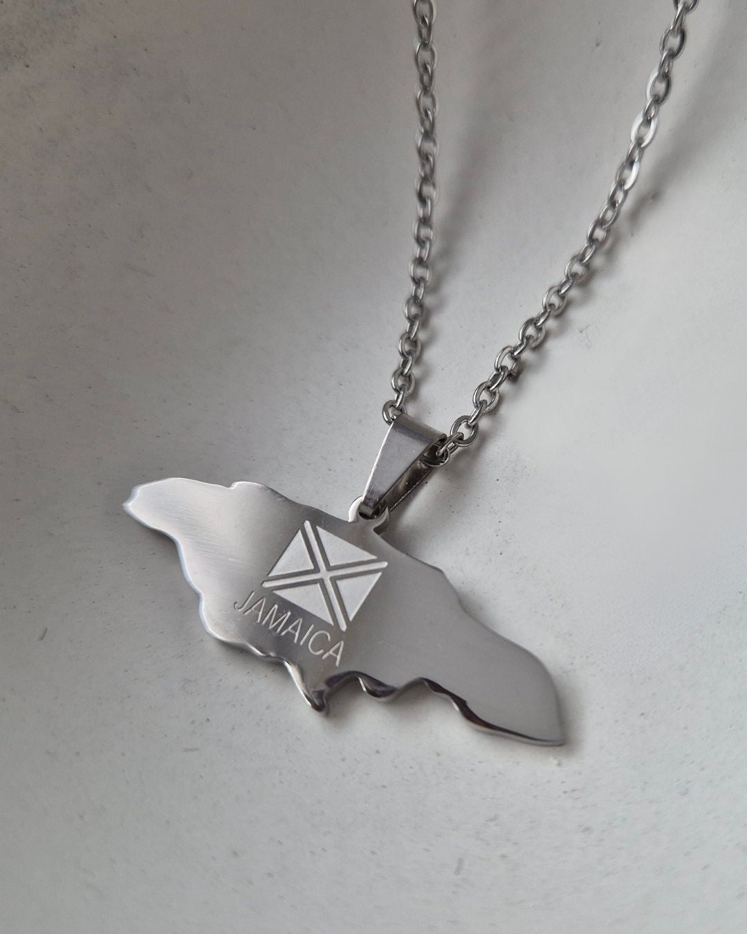 Silver necklace with a pendant shaped like Jamaica on a light gray background