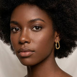 Woman with an afro hairstyle wearing gold earrings against a plain background