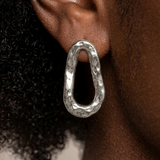Silver earrings worn by a person with curly hair on a neutral background