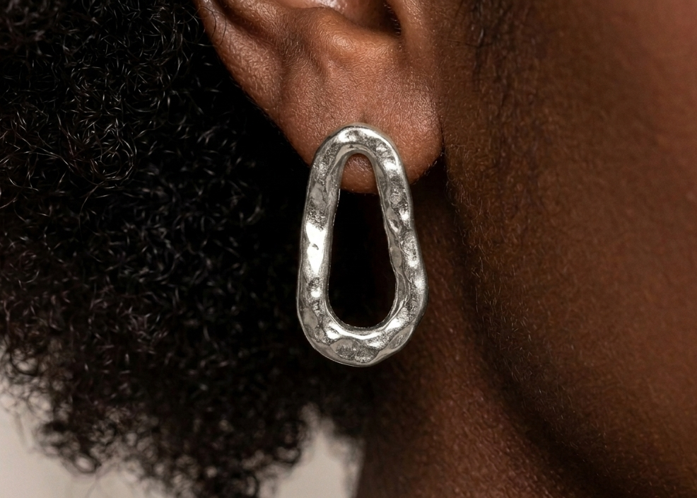 Silver earrings worn by a person with curly hair on a neutral background