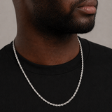 Man wearing a silver chain necklace against a neutral background