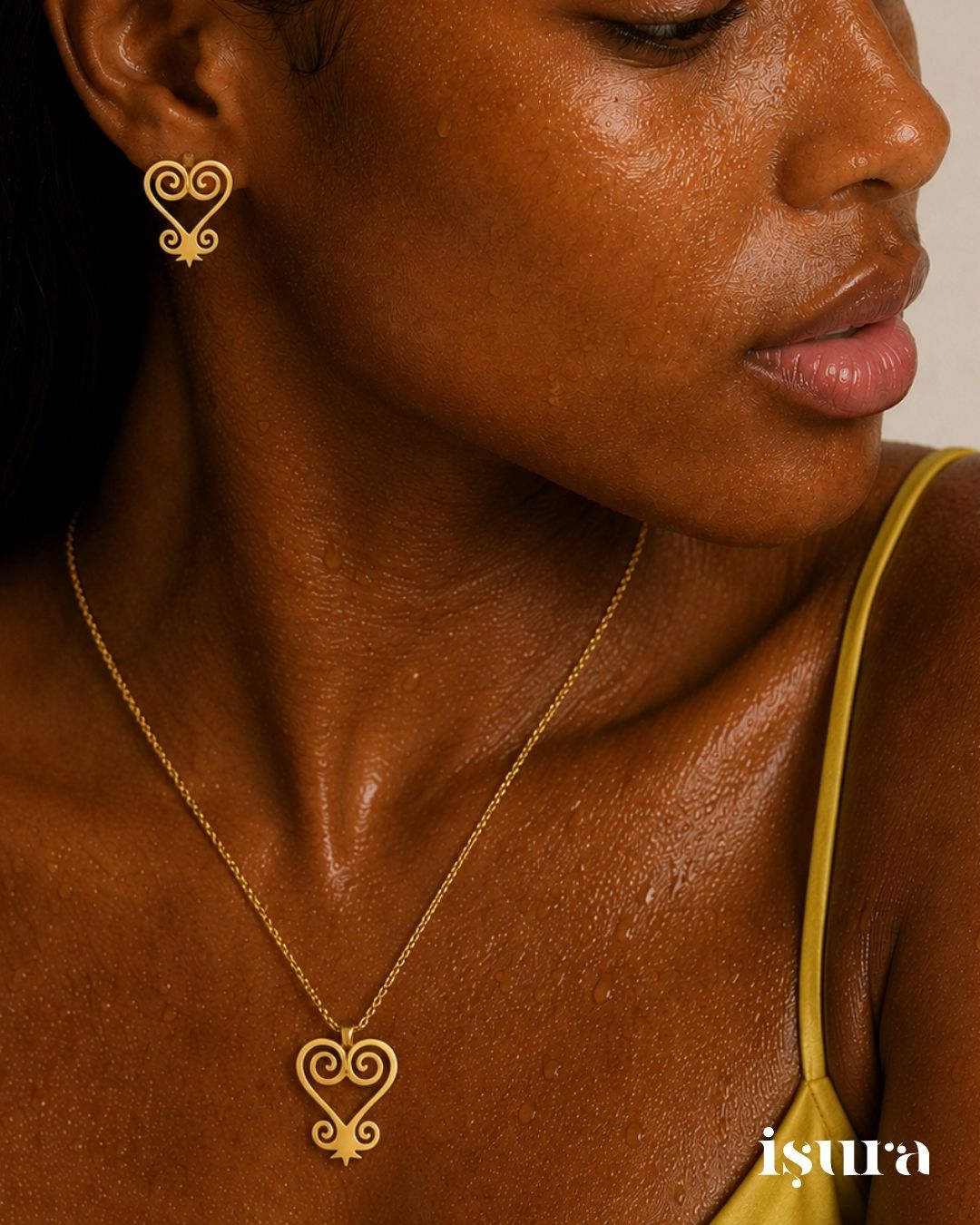 Close-up of a person wearing a gold earring and necklace with 'isura' branding.