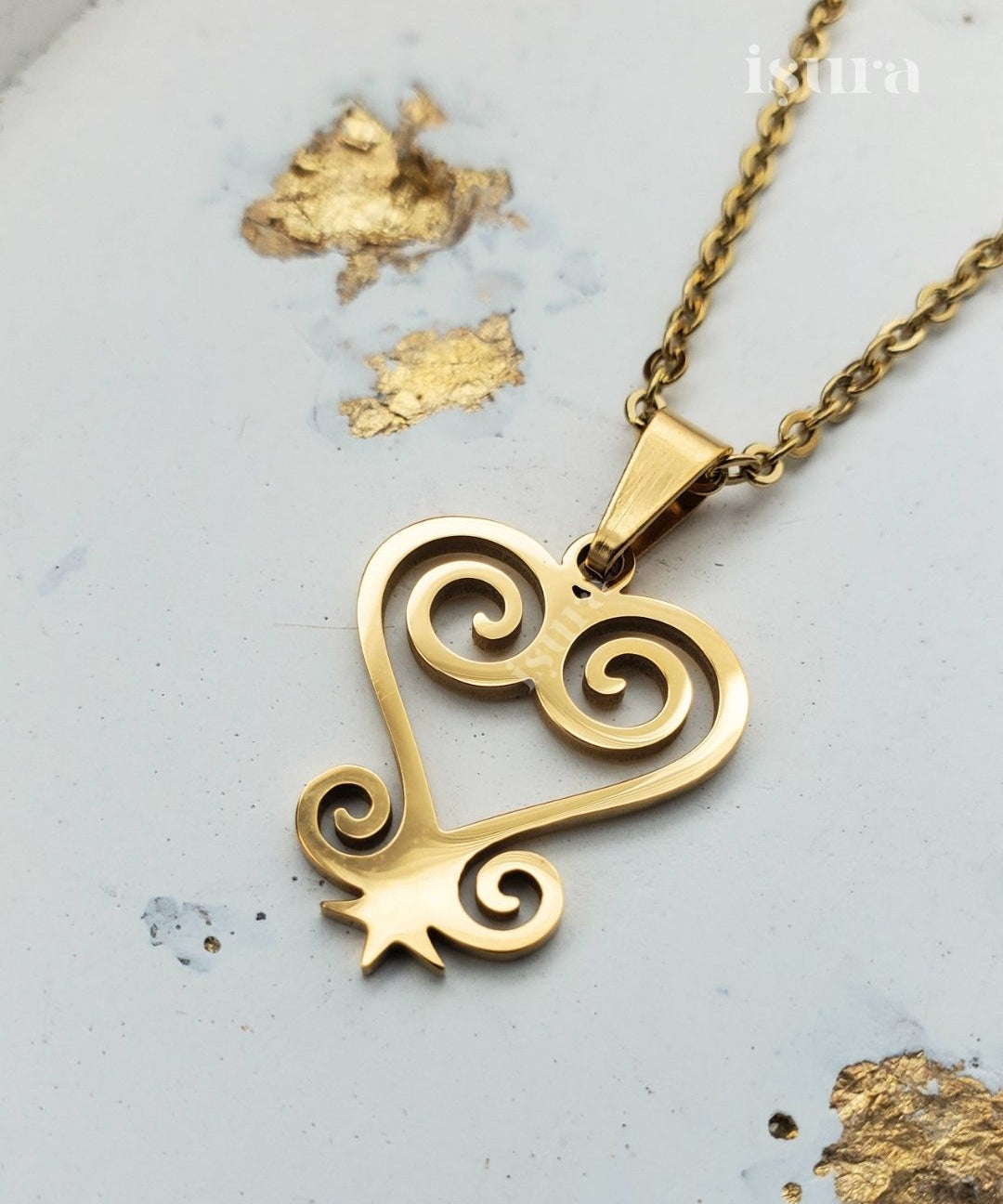 Gold heart-shaped pendant necklace on a light gray background with gold leaf accents.
