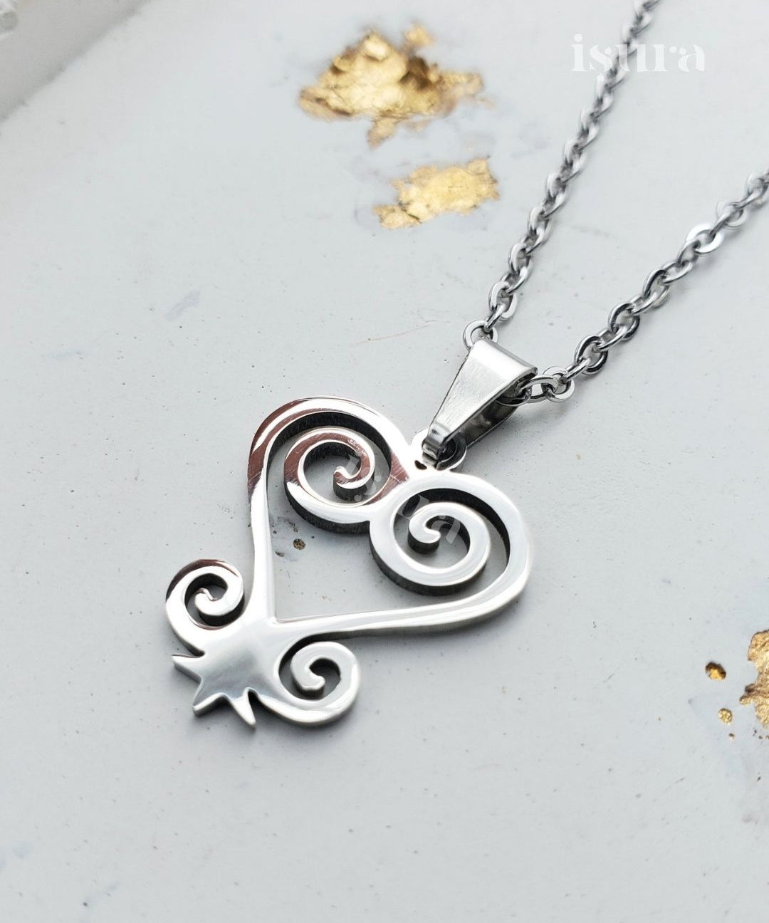 Silver heart-shaped pendant with intricate designs on a chain against a light gray background.